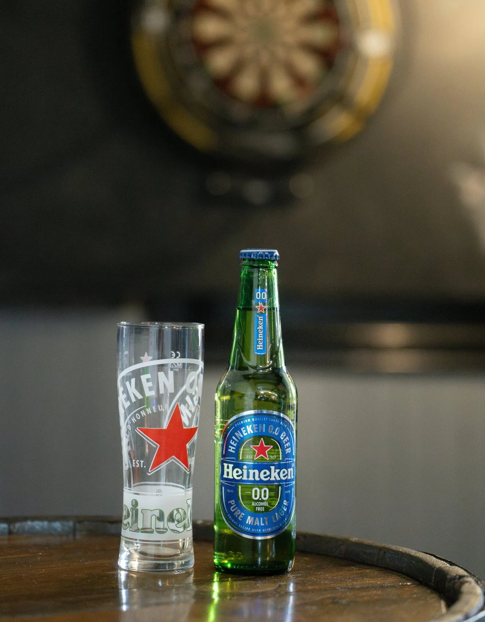 A bottle and glass on a barrel table, the dartboard softly out of focus on the wall behind