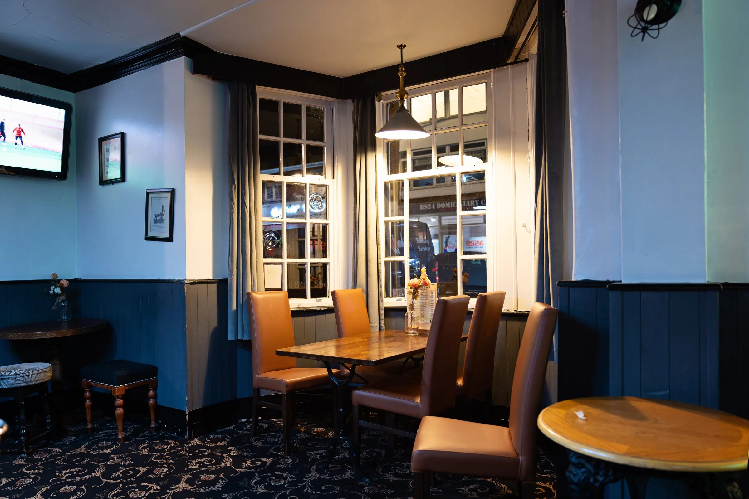 The lounge — leather chairs round wooden tables by the window, the match on the television in the corner