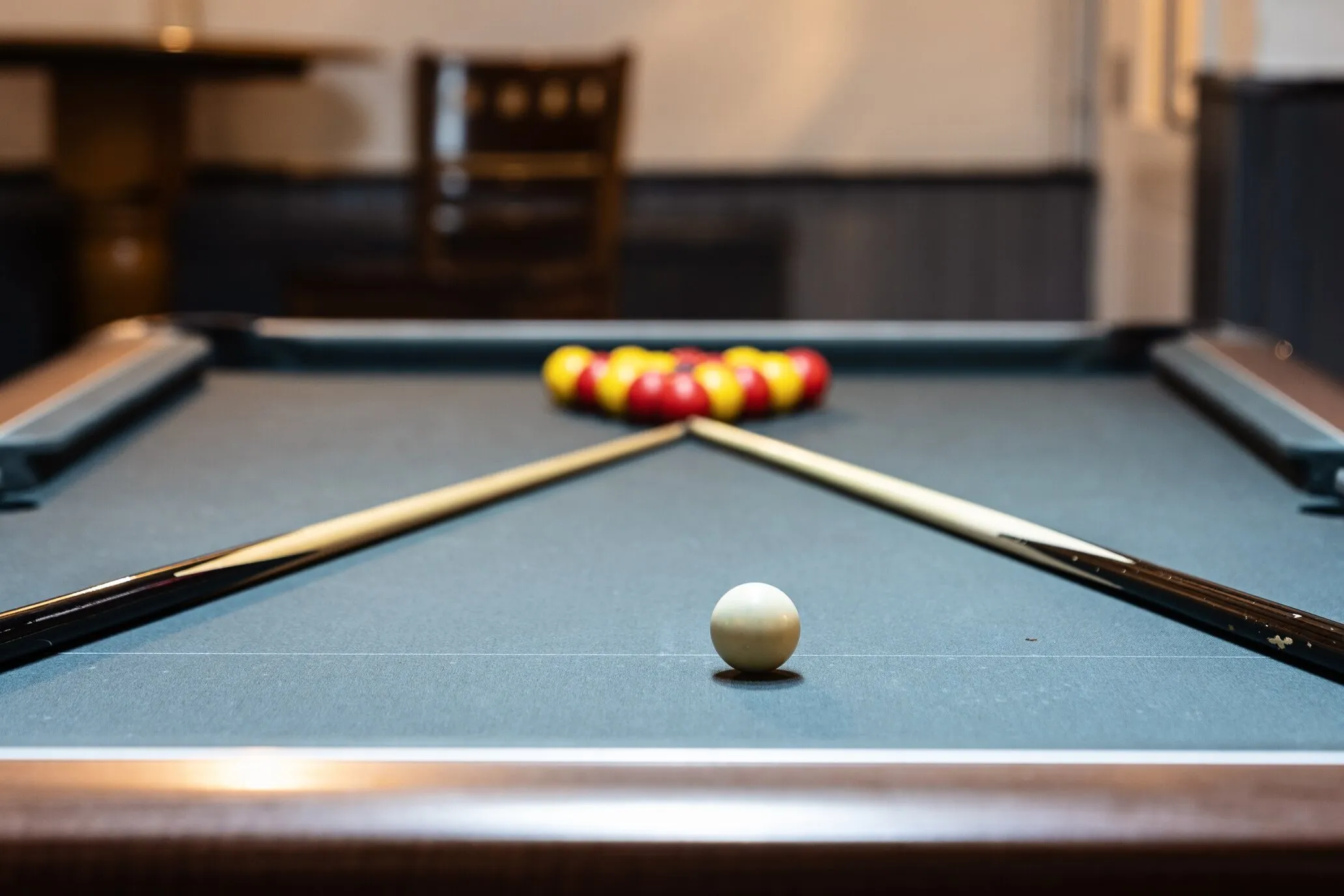 The pool table racked for a break, cue ball in sharp focus and two cues resting on the cloth